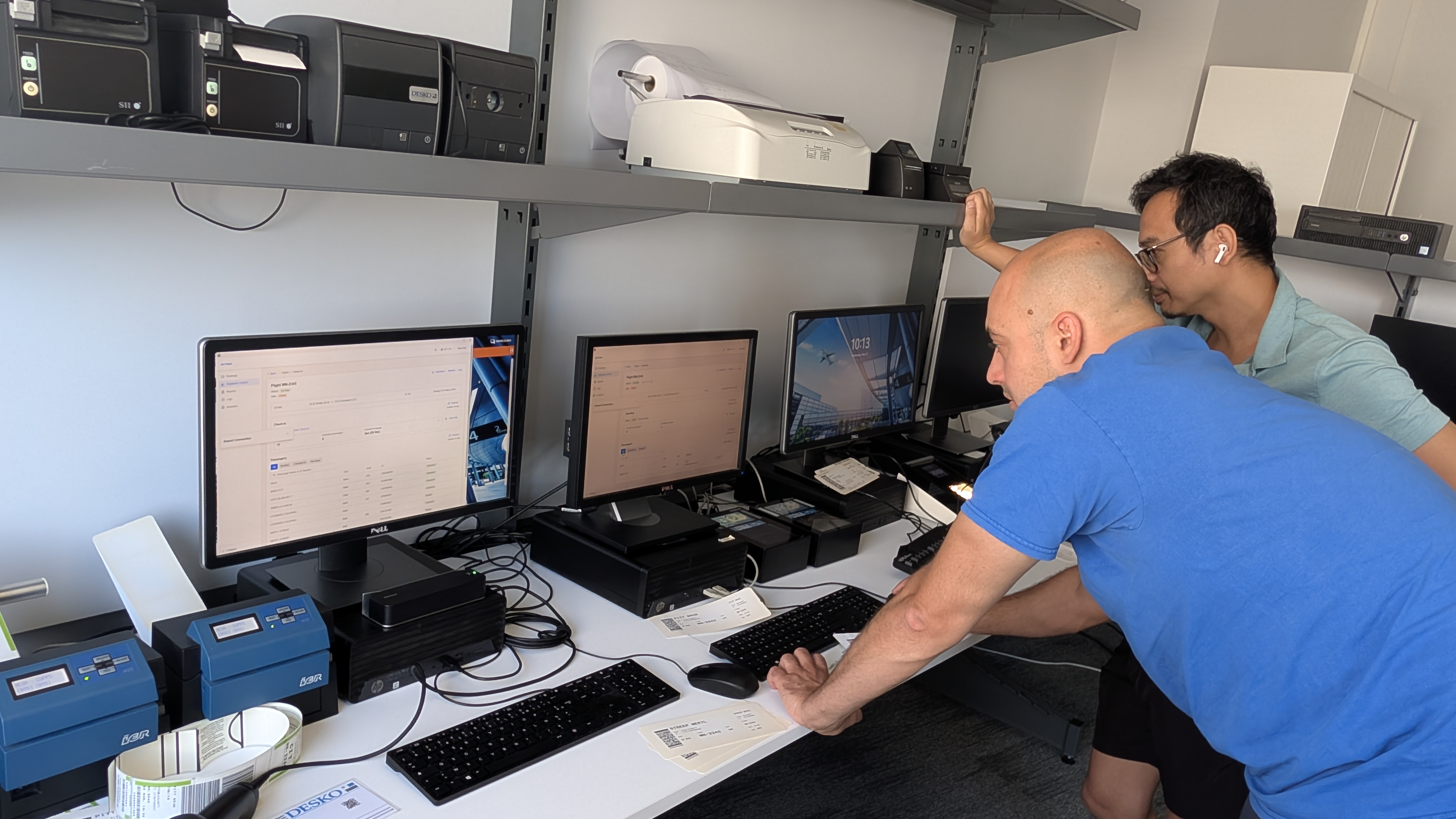 A Farel engineer and a RESA engineer running CUTE certification at RESA's lab, with common-use bag-tag printers, document scanners, and boarding-pass printers on the test bench.