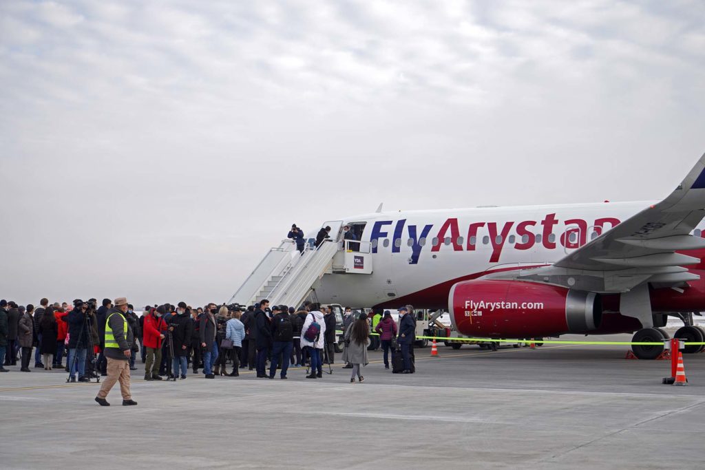Crowd of press and passengers boarding a FlyArystan A320 via airstairs at the apron